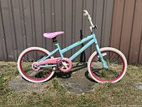 Side view of bike showing teal frame, pink pedals, pink tire rims and white tires.