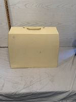 Beige carrying case closed, front view on table with background and measuring stick.