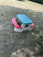 Image showing the plastic kids picnic table on grass from a side angle, highlighting the white base, red benches, and teal tabletop.