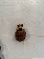 Front view of the monkey in barrel cookie jar on white fabric with wood panel background.