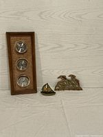 Nautical-themed lot displaying a wooden weather station with three round metal dials, a small brass sailboat with stained glass sails, and a brass decorative piece of birds on waves with stained glass.