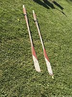 Pair of wooden boat oars laid on grass surface showing entire length and painted blades with heavy wear.