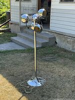 Full view of the chrome five headed retro lamp standing on grass outside, showing the round weighted base and five spherical lamp heads clustered at the top of the pole.