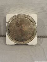 Silver-colored round serving tray in styrofoam base, showing tarnished surface with beaded edge detail.