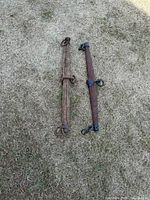 Two wooden yokes laying on dry grass, showing full length and metal attachments.