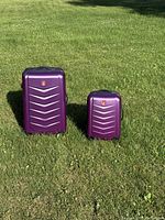 Two purple suitcases in standing position on grass, front view showing size comparison.