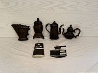 Top view of five decorative plastic wall plaques showing the potbelly stove, coffee pot, coffee grinder, tea pot, and butter mold arranged on a wooden surface.