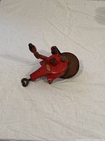 Vintage red metal HOPPE hand grinder with crank handle and grinding stone wheel showing wear and rust, placed on white fabric background.