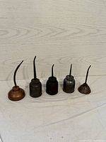 Front view of the five vintage oil cans arranged in size order from tallest to smallest on a white surface against wood panel background.
