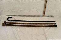 Three wooden walking aids displayed horizontally with a measuring ruler above them showing length.