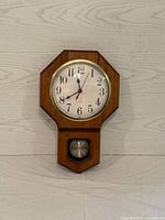 Front view of wooden pendulum clock showing full clock face and pendulum window.