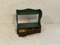 Wooden trinket shelf showing front and three pullout drawers.