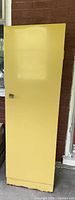 Closed yellow metal cabinet showing plain door with metal handle and scuffed lower edge.