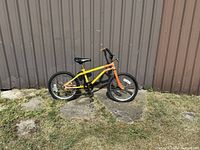Side view of the young teen bike showing yellow frame and orange front fork, black tires, and padded black seat.