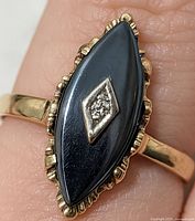 Top view on finger showing marquise hematite stone, scalloped gold bezel and central diamond.