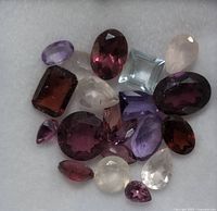 Top-down view of assorted genuine faceted gemstones of various colors and cuts on a white felt background.