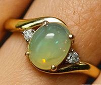 Ring on finger showing oval opal and side diamonds