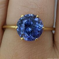 Top-down view of the round faceted tanzanite and six-prong gold setting on finger