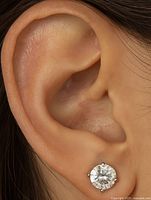 Close-up photo showing one of the stud earrings worn on an ear, highlighting the clear round moissanite stone set in 14K gold with four prongs.