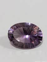 Oval faceted purple amethyst gemstone placed against white background showing color and cut.