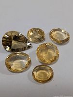 Six loose faceted citrine gemstones in various cuts and yellow tones on white background