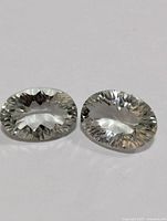 Two oval cut green amethyst gemstones placed on white background, showing clarity and cut facets.