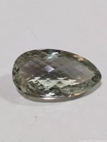 Close-up of genuine green amethyst gemstone cut in a pear shape showing its facets and clarity.