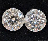 Close-up photo of two round cut moissanite stones on black fabric, showing clarity and faceting