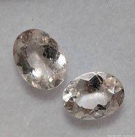 Two oval cut colorless moissanite gemstones shown side by side on a light background, highlighting faceting and transparency.