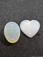 Two polished opal gemstones including an oval and a heart shape on black background.
