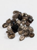 Collection of faceted genuine smokey quartz gemstones of varying shapes and sizes shown on white background.