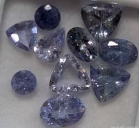 Multiple tanzanite gemstones of different cuts and sizes displayed on a white background.