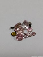 Loose assorted faceted tourmaline gemstones of various sizes and colors against a plain background.