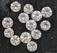 Close-up view of clear white round cut sapphire gemstones on a black surface, showing brilliance and cut details.