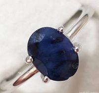 Close-up front view of sterling silver ring with oval blue sapphire stone showing prong setting and stone details.