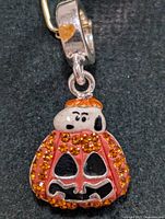 Front view of the Halloween Snoopy pumpkin charm attached to the bracelet showing details of orange rhinestones and enamel work on the pumpkin and Snoopy's head.