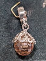 Close-up photo of sterling silver charm with orange faceted bead and silver scrollwork cap, showing bail and hanging loop.