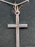 Front view of sterling silver cross pendant showing detailed starburst engraving on a box chain.