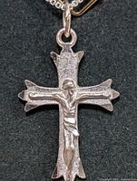 Close-up photo of the silver crucifix pendant on the necklace showing textured cross and detailed Jesus figure, against black background.