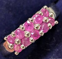 Close-up angled photo of silver ring showing two rows of faceted round pinkish-red rubies held by silver bead prongs on silver band, highlighting the stones and setting detail.