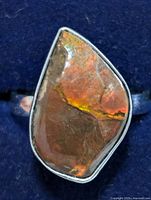Close-up view of silver ring with polished Canadian ammolite gemstone showing orange-brown iridescence and natural surface texture.