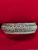 Front side view of the sterling silver ring showcasing the wide band with chain link design and rope border details against a red background.