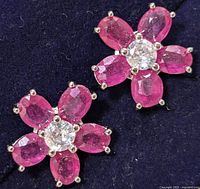 Front view of two ruby flower earrings showing five faceted ruby petals and central clear gemstone per earring.