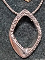 Close-up front view of diamond-encrusted silver pendant on snake chain necklace showing shape and setting of diamonds.