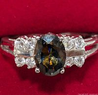 Close-up front view of silver ring with dark oval central stone and marcasite accents on a red background.