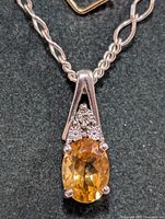 Close up front view of the pendant showing the oval citrine stone surrounded by silver and three small diamonds on top.