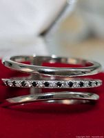 Close up photo of the silver ring on red fabric showing the clear cubic zirconia stones embedded in the central narrow band and the two plain silver bands above and below it.