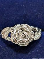 Close-up image of sterling silver ring with rose flower and leaf design on band, showing front view
