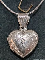 Close-up of the sterling silver heart-shaped locket pendant showing the engraved pattern on the front.