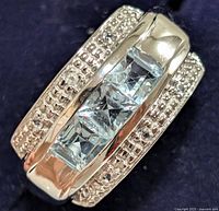 Close-up image of the sterling silver ring showing the side view with three square-cut blue white topaz stones and milgrain detailing on edges.